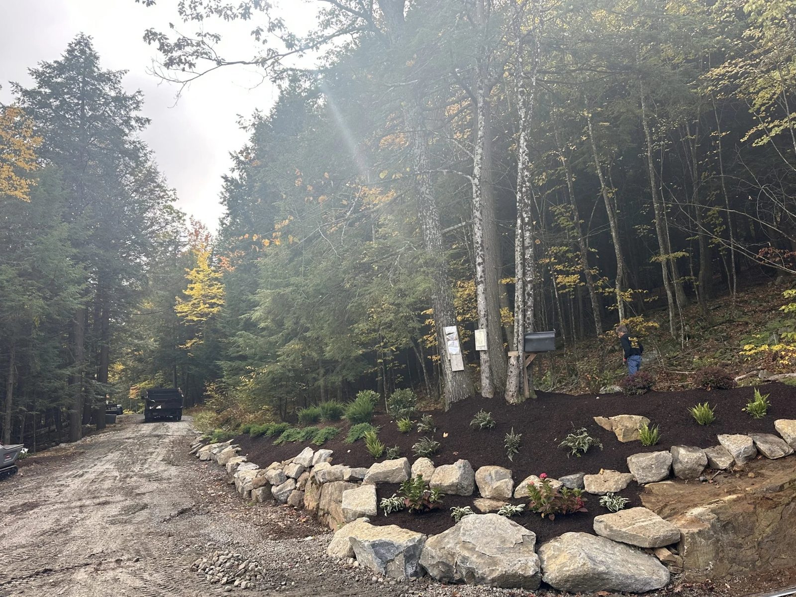 Boulder retaining wall and planting bed along a wooded driveway