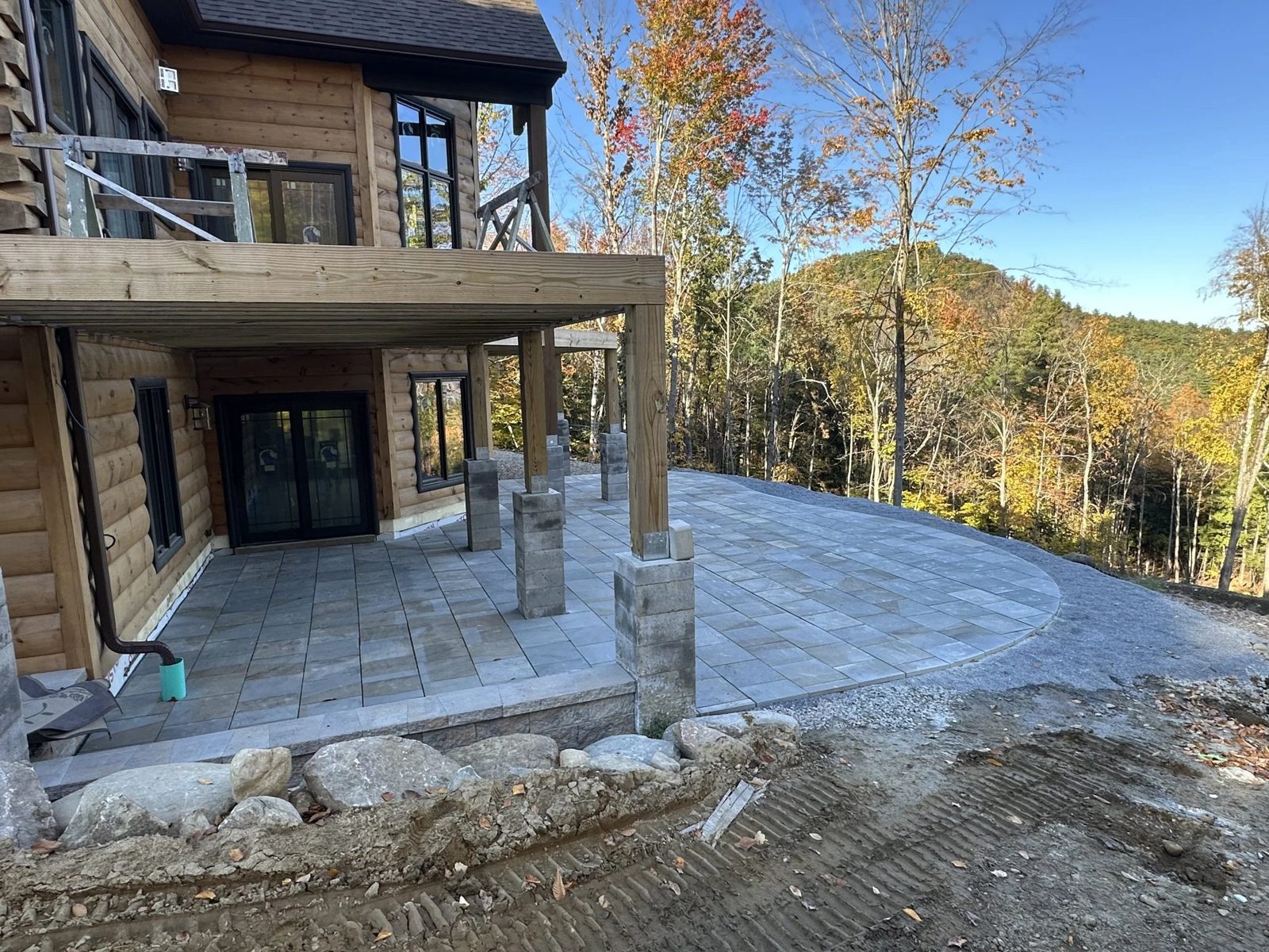 Large-format gray paver patio under a log cabin deck with mountain views
